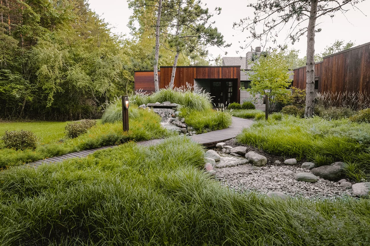 Image of a front yard landscape project showing a walkway and a stone water feature in a natural setting designed by Walden Design from Rockford MI